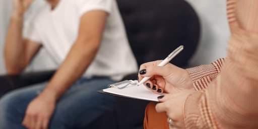 zdjęcie przedstawia terapeutkę z notesem oraz pacjenta siedzących naprzeciwko siebie